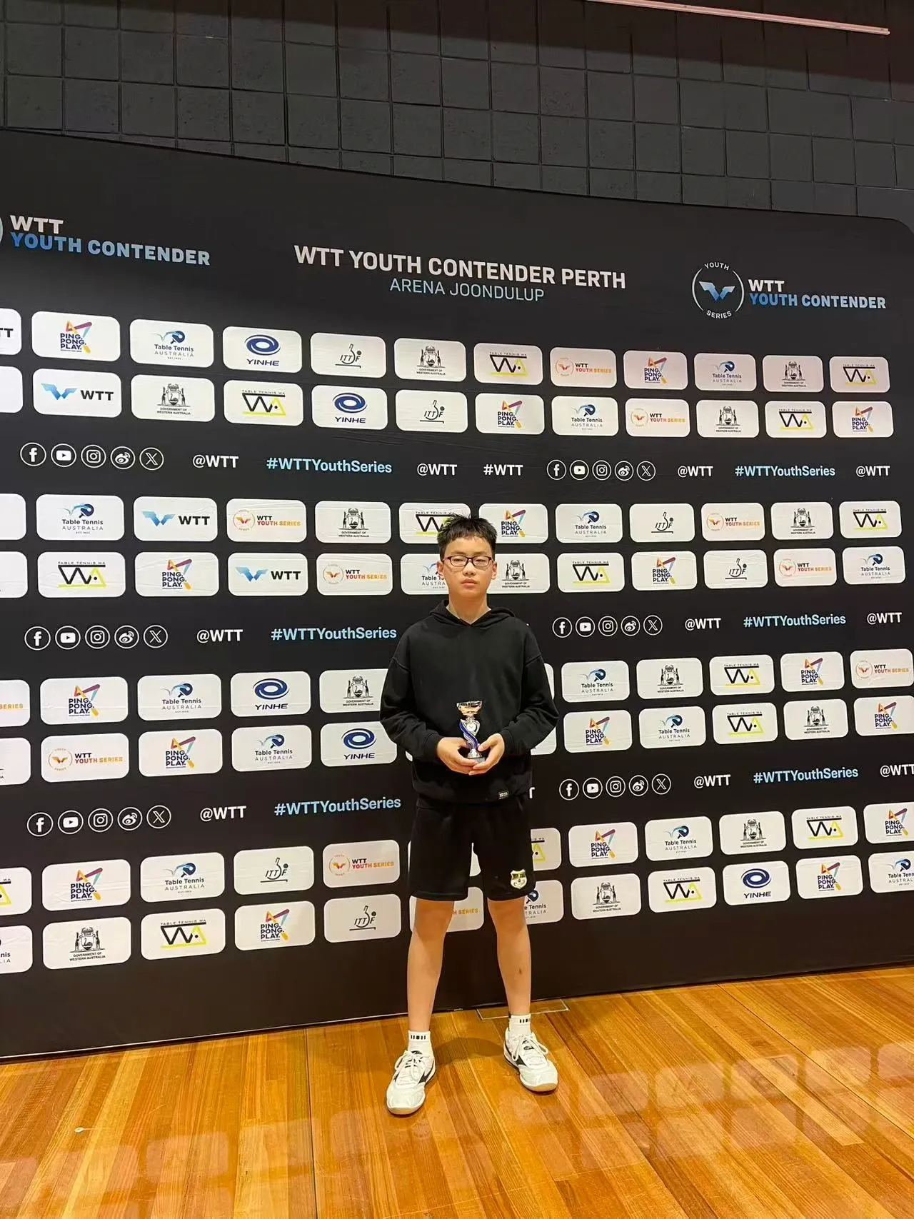 Lachlan Bao 在 WTT Youth Contender Perth 赛事背景前持奖杯合影