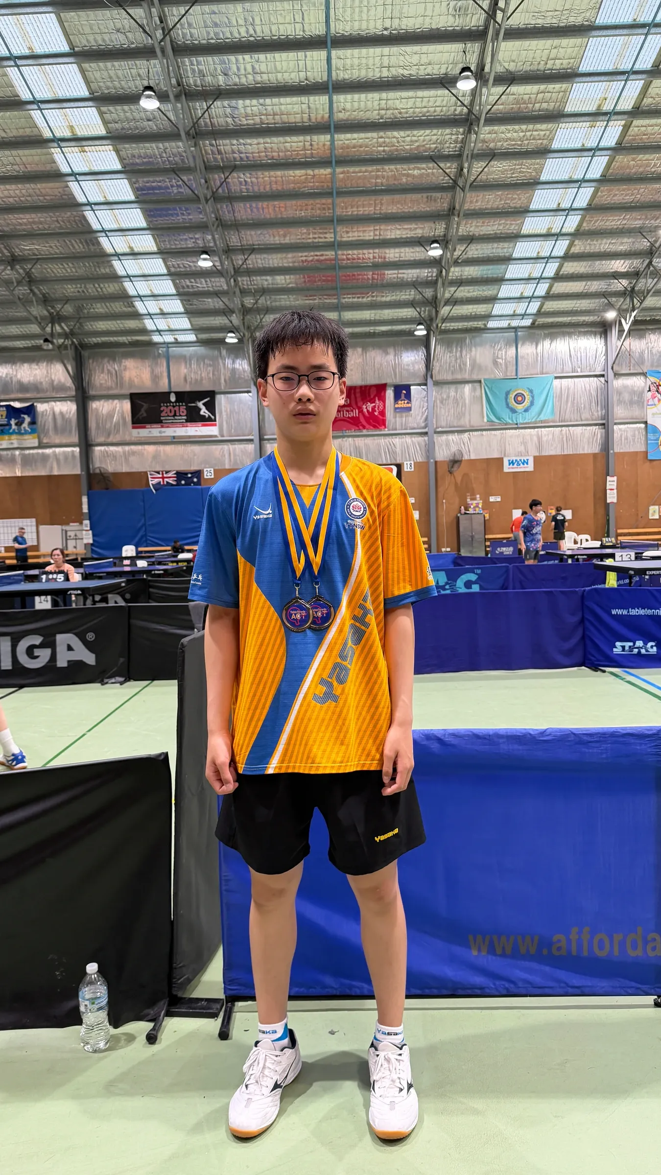Lachlan Bao 身穿新南威尔士州队服，在乒乓球赛场佩戴奖牌